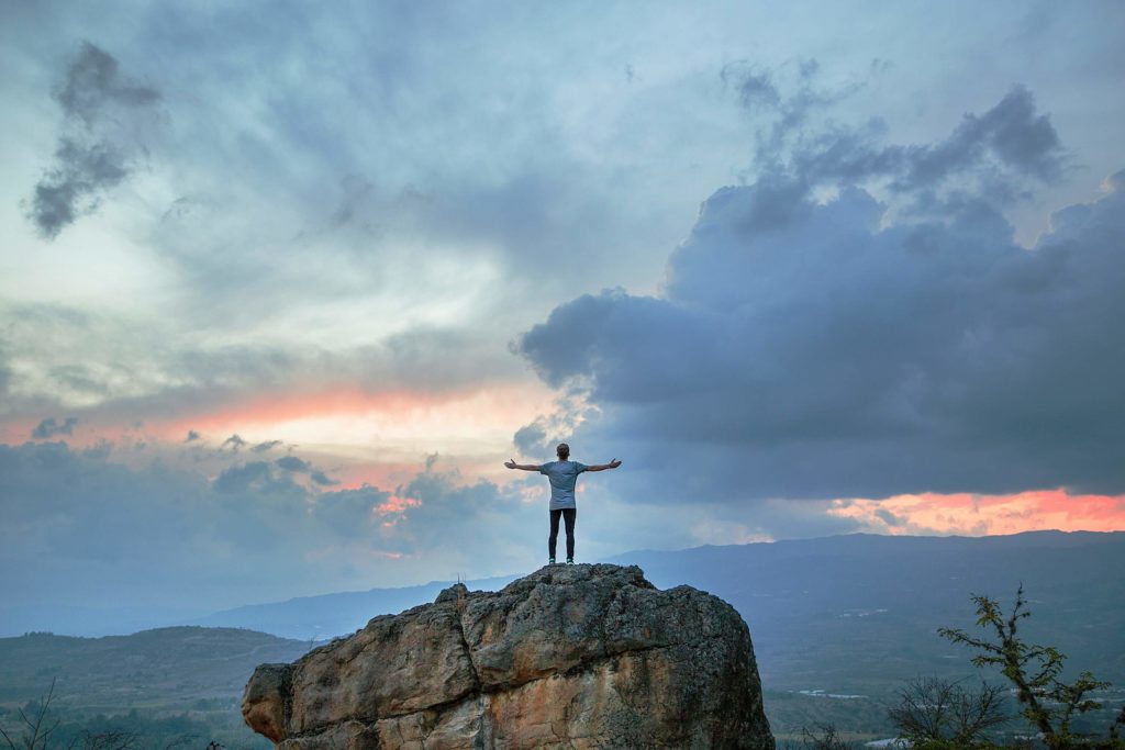 Image of a man standing on top of a rock with his arms raised feeling free. Work to overcome the challenges you face after a major life change with  the help of life transition therapy in Austin, TX.