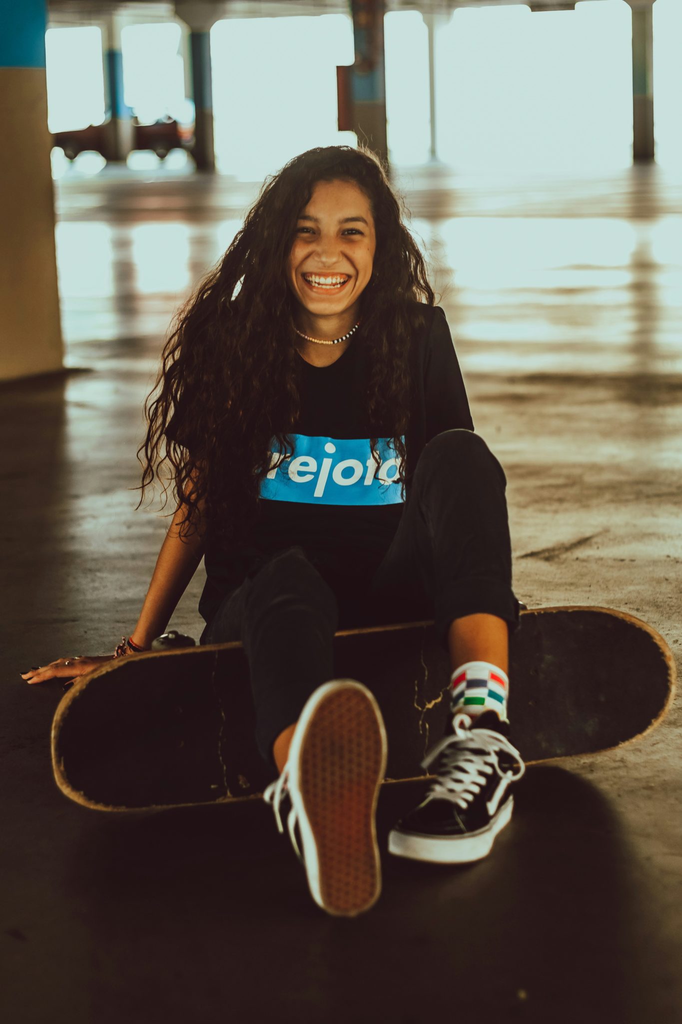 Image of a teen girl smiling and holding a skateboard while sitting on the ground. If you are struggling with a major life change, learn how life transitions therapy in Austin, TX can help.