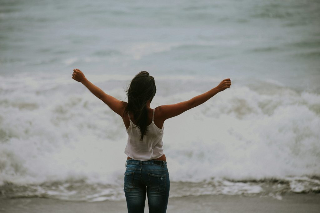 Image of a woman standing on the beach with her arms in the air. This image represents the feeling of freedom after managing your life with life transitions therapy in Austin, TX.