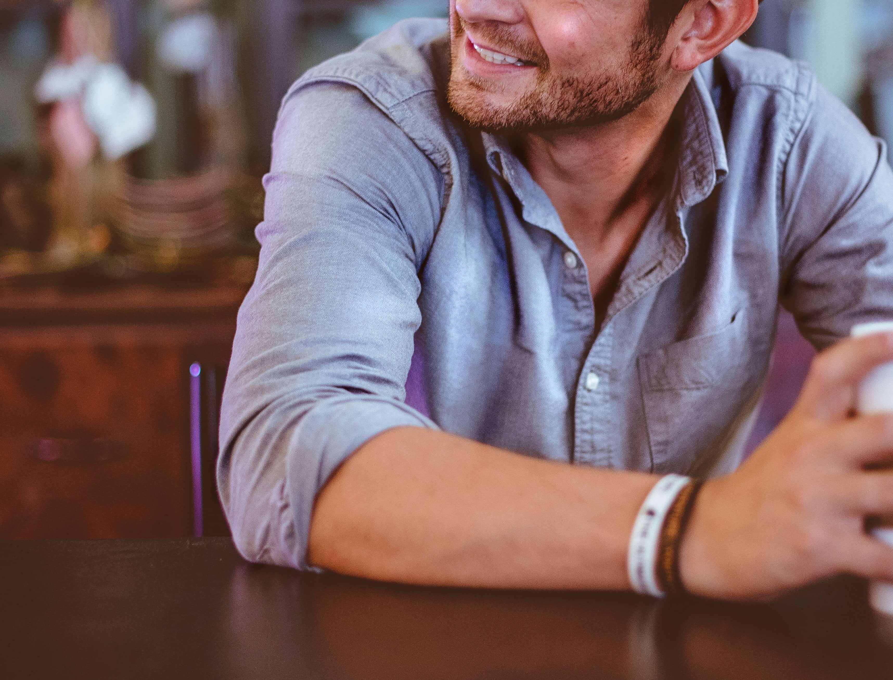 Image of a smiling man sitting at a table holding a coffee mug. Find support navigating your major life changes with the help of life transitions counseling in Austin, TX.