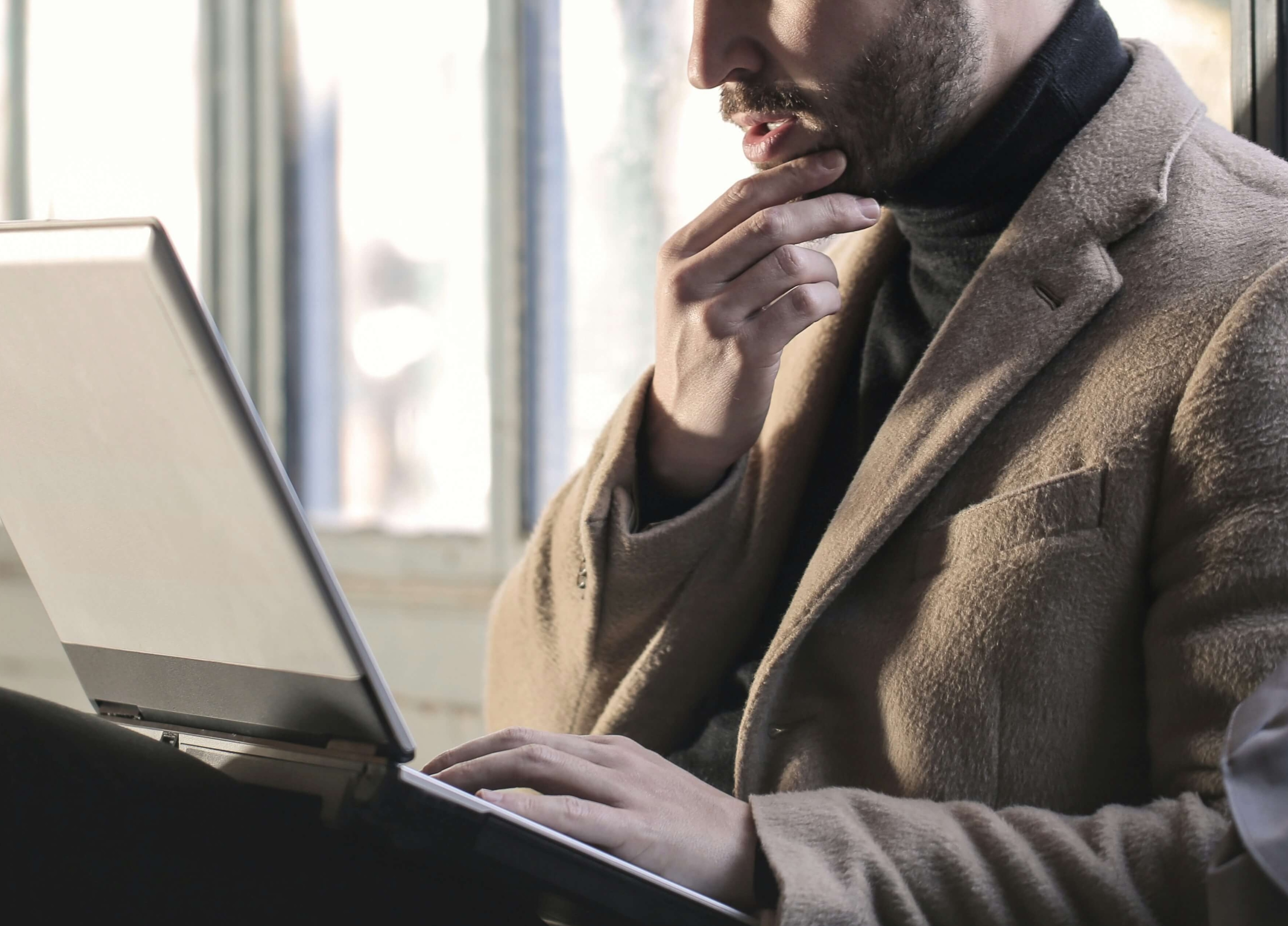 Image of a man touching his chin in thought while working on a laptop. Coping with major life changes doesn't have to be difficult. With the help of life transition therapy in Austin, TX you can cope with change in healthy ways.