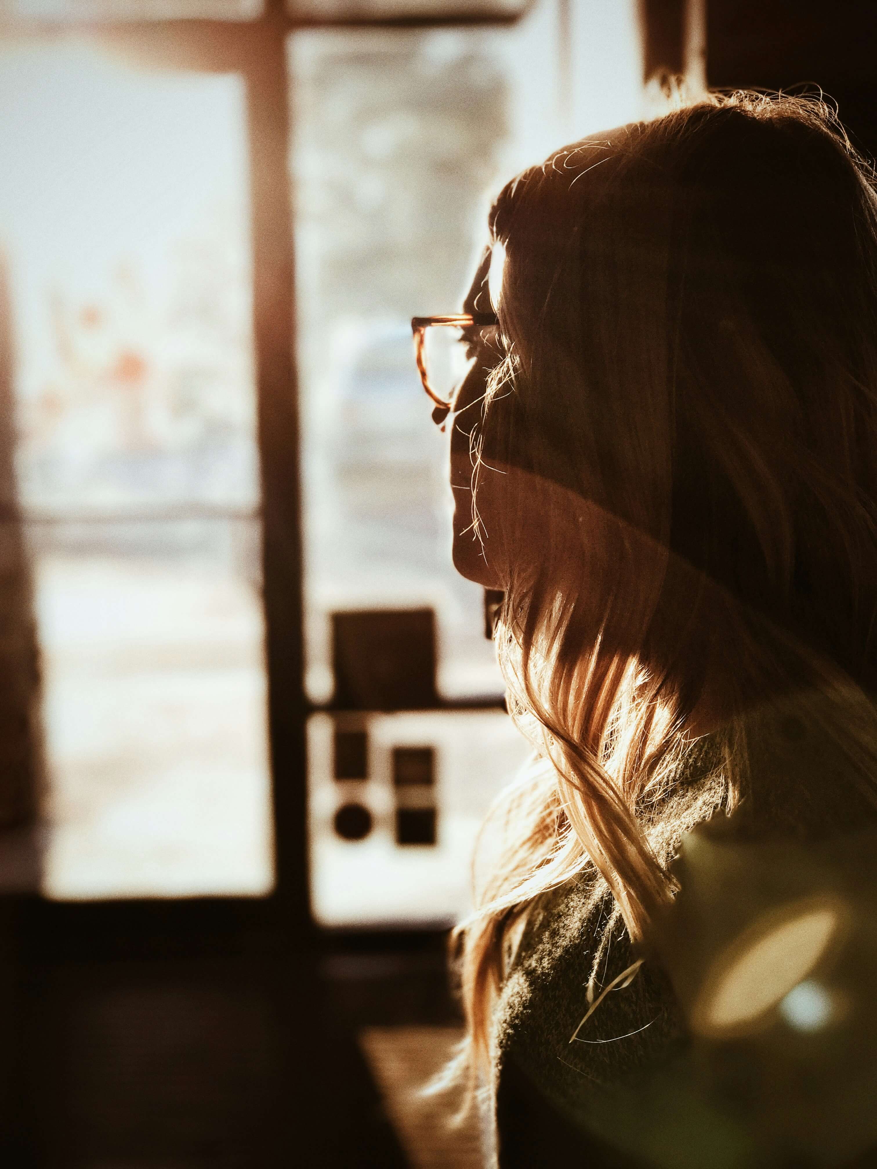 Image of a woman wearing glasses looking out a window. If you are going through a major life change, find support with life transition therapy in Austin, TX.