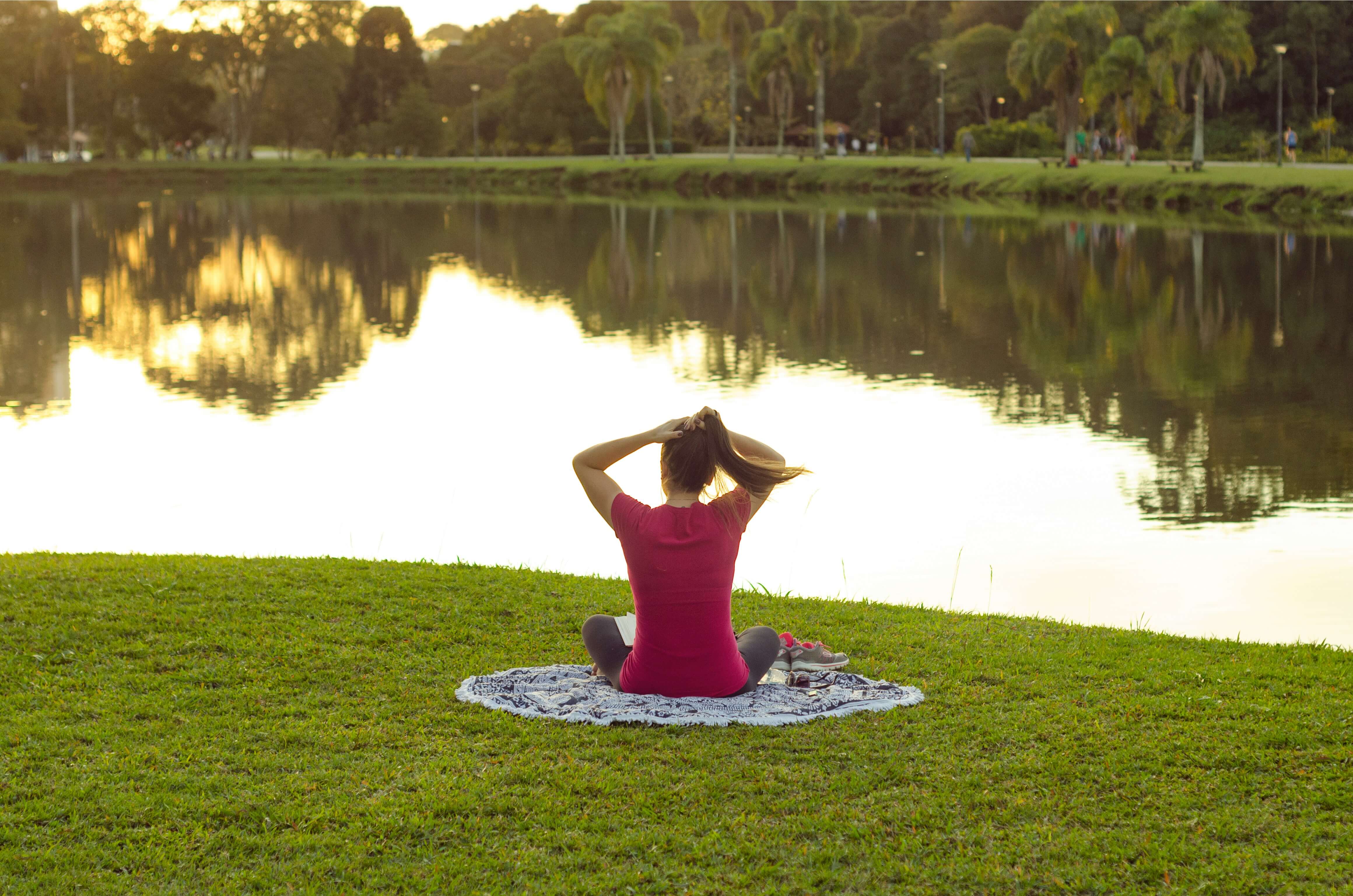 Image of a woman sitting on a blanket by a pond in a park. If you are struggling to cope with the challenges that come with life transitions, learn how life transition therapy in Austin, TX can help you.