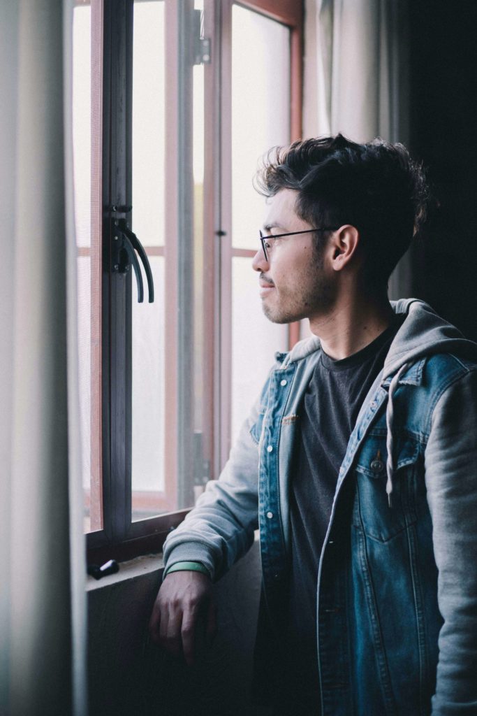 Image of a man wearing glasses looking out a window. Discover how life transition therapy in Austin, TX can help you adjust and cope with major life changes.