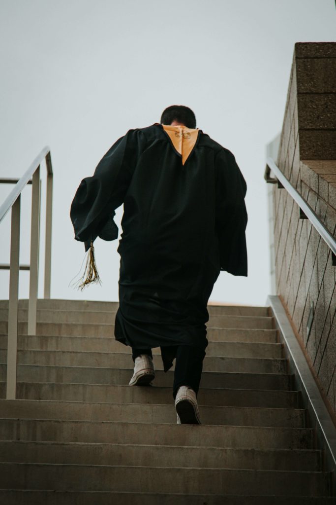 Image of a student wearing graduation robe and holding a hat walking up the stairs. Learn to adjust the transition to adulthood with the help of life transition therapy in Austin, TX.