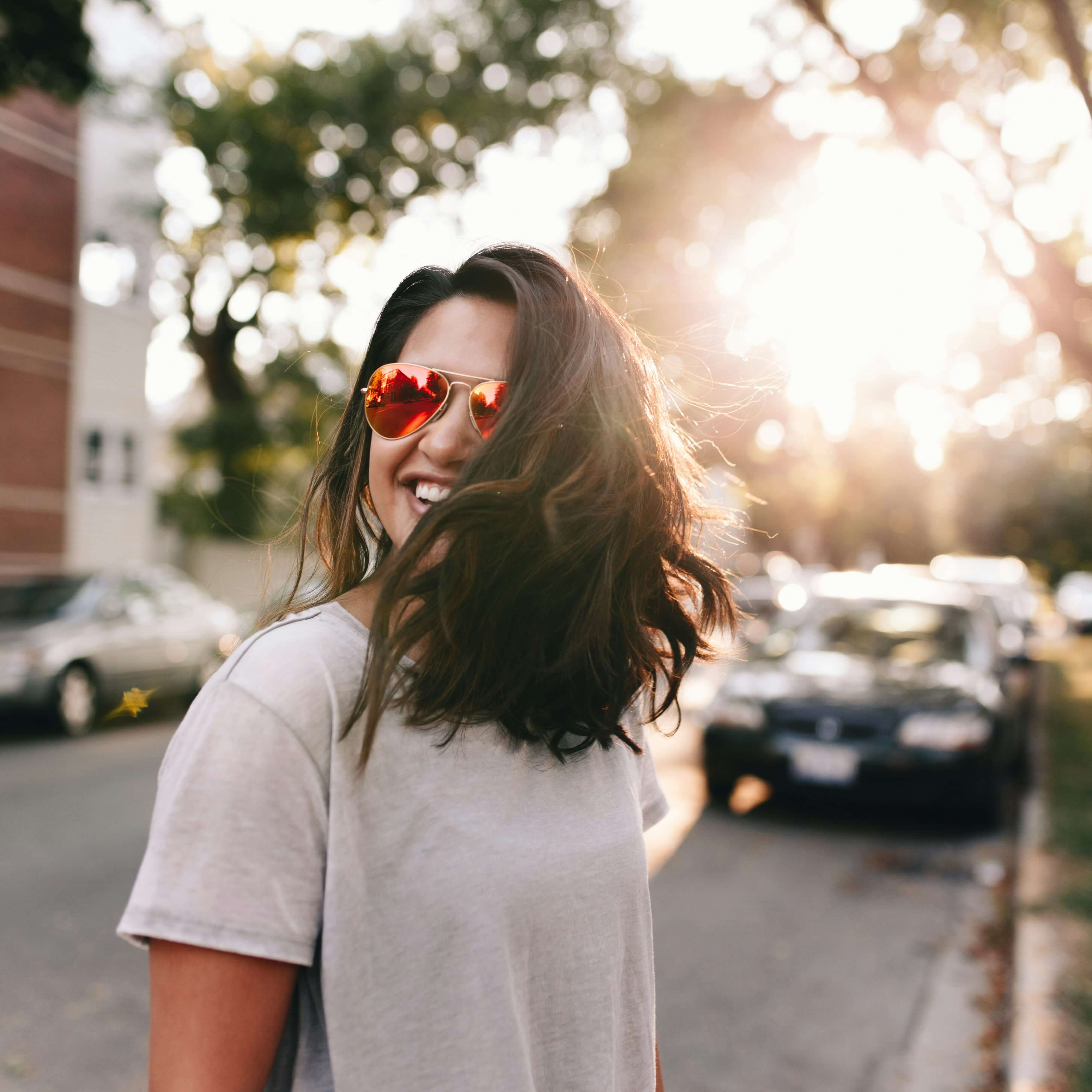 Image of a smiling woman standing in the street wearing sunglasses. If you are dealing with a major life change, learn how life transitions therapy in Austin, TX can help you adjust to change.