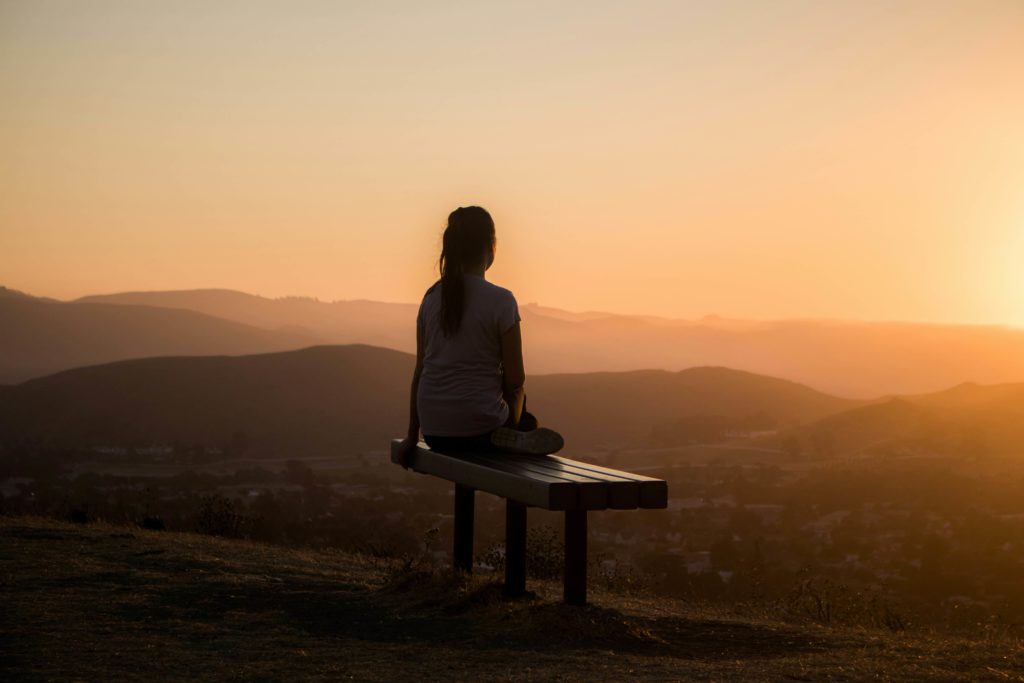 Image of a woman sitting on a bench looking at the sunrise. If you are struggling with a major life change, learn how life transitions therapy in Austin, TX can help you cope.