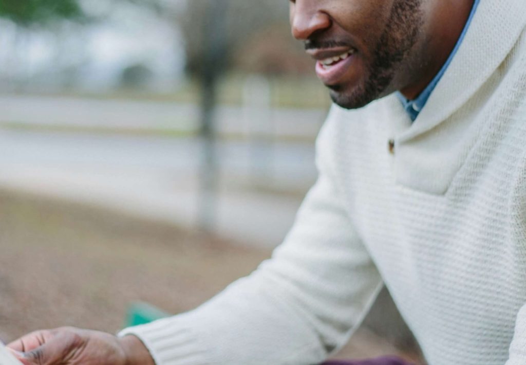 Image of a smiling man sitting on a bench reading. Discover how to navigate transitions in adulthood with the help of life transitions therapy in Austin, TX.